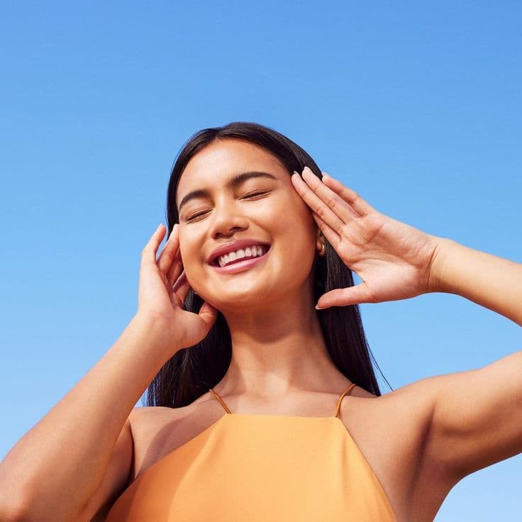 Smiling woman with her eyes closed against a clear blue sky